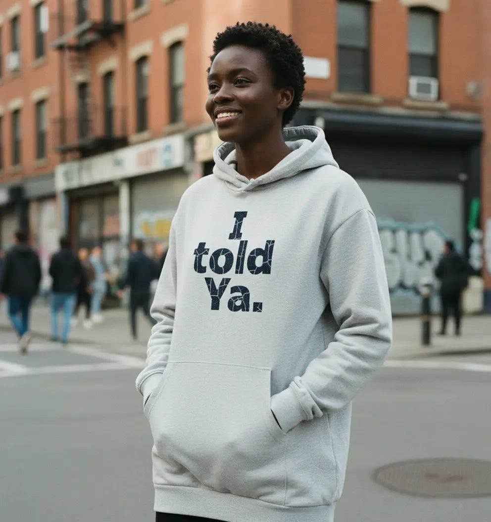 Woman wearing a light grey Nova Hoodie Dress with "I told Ya." text, standing on a city street.